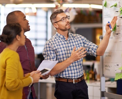 Man gesturing to whiteboard with two colleagues