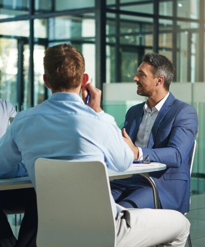 3 men wearing business clothes talking around a table in an office
